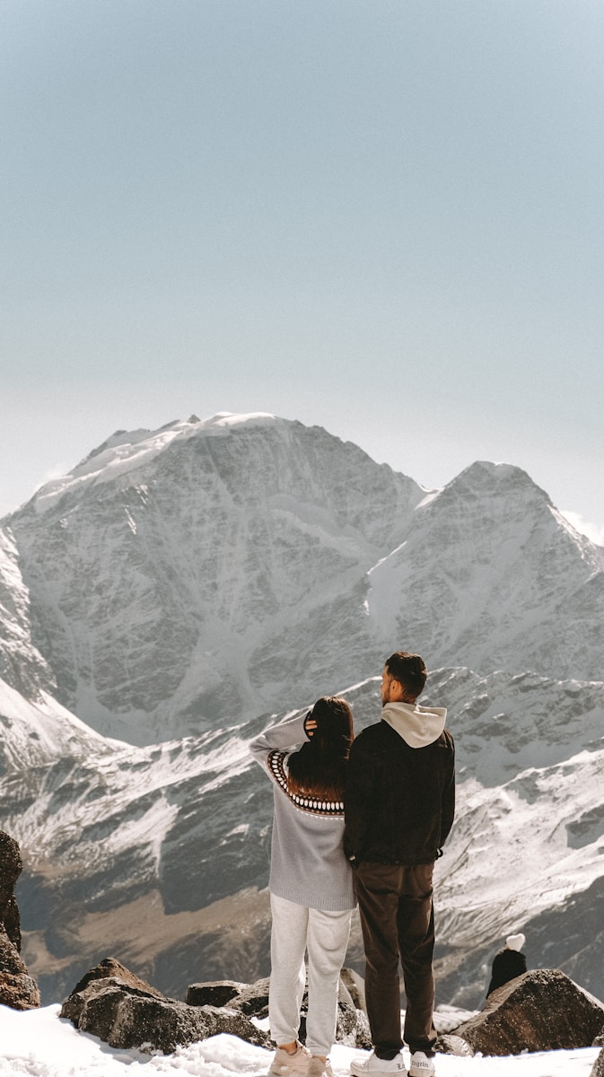 a man and woman standing on a mountain top with a mountain in the background