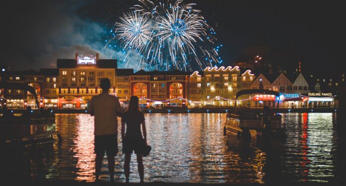 two people standing beside body of water watching fireworks