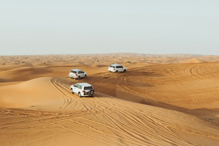 three white vehicles moving in desert under gray sky